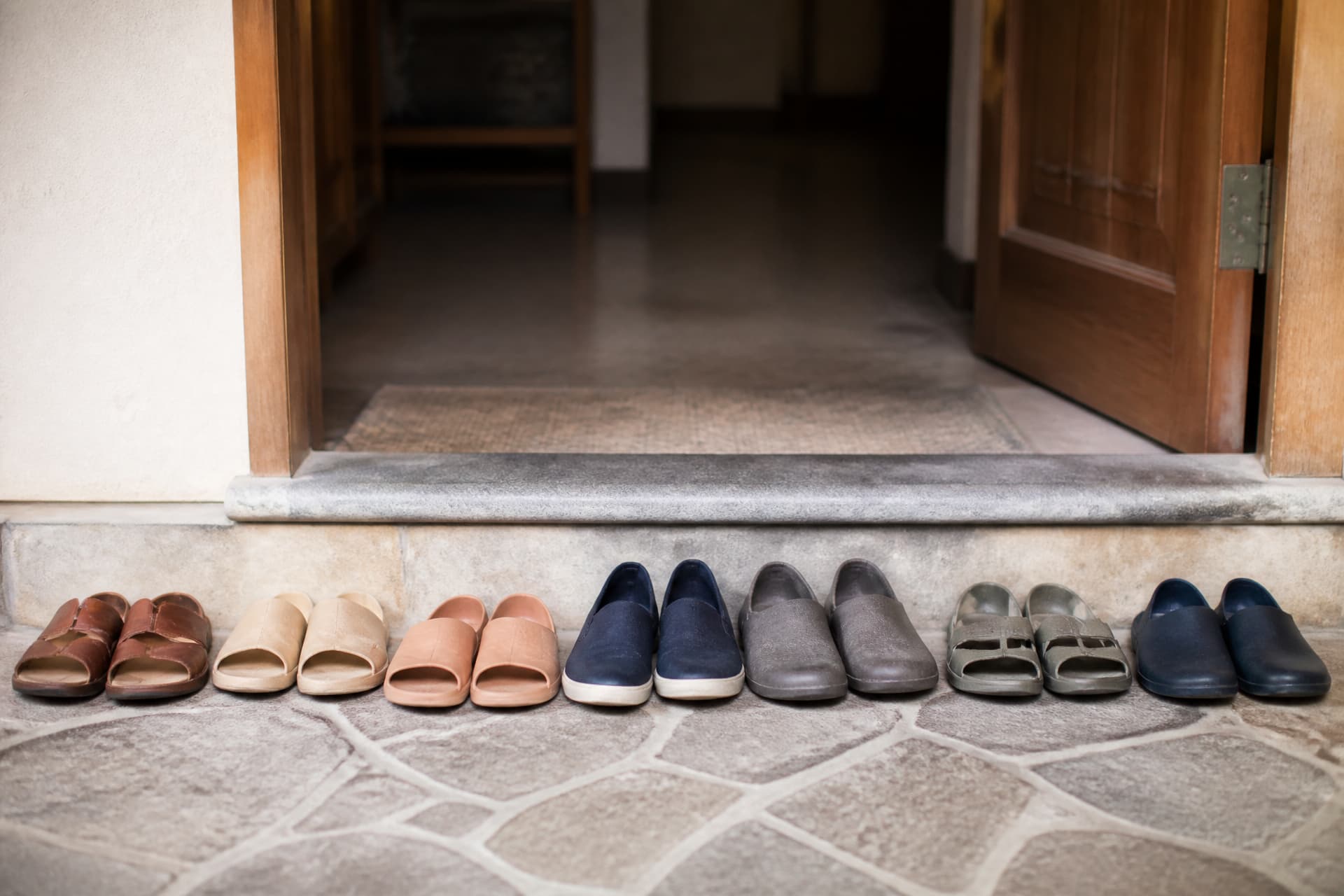 Several pairs of plain slip-on shoes left neatly in a row outside a doorway