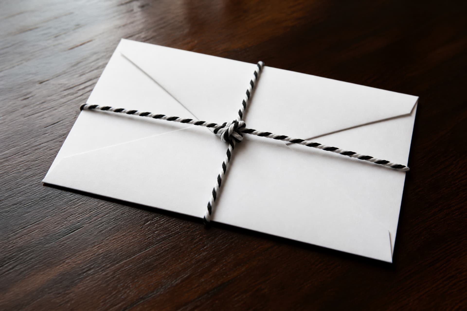 A plain white condolence envelope tied with black and white cords resting on a dark wooden table