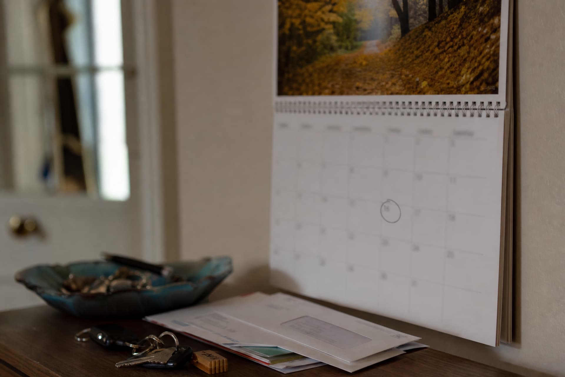 A wall calendar turned to an autumn month with one date circled in pencil, hanging above a cluttered hall table with keys and unopened mail