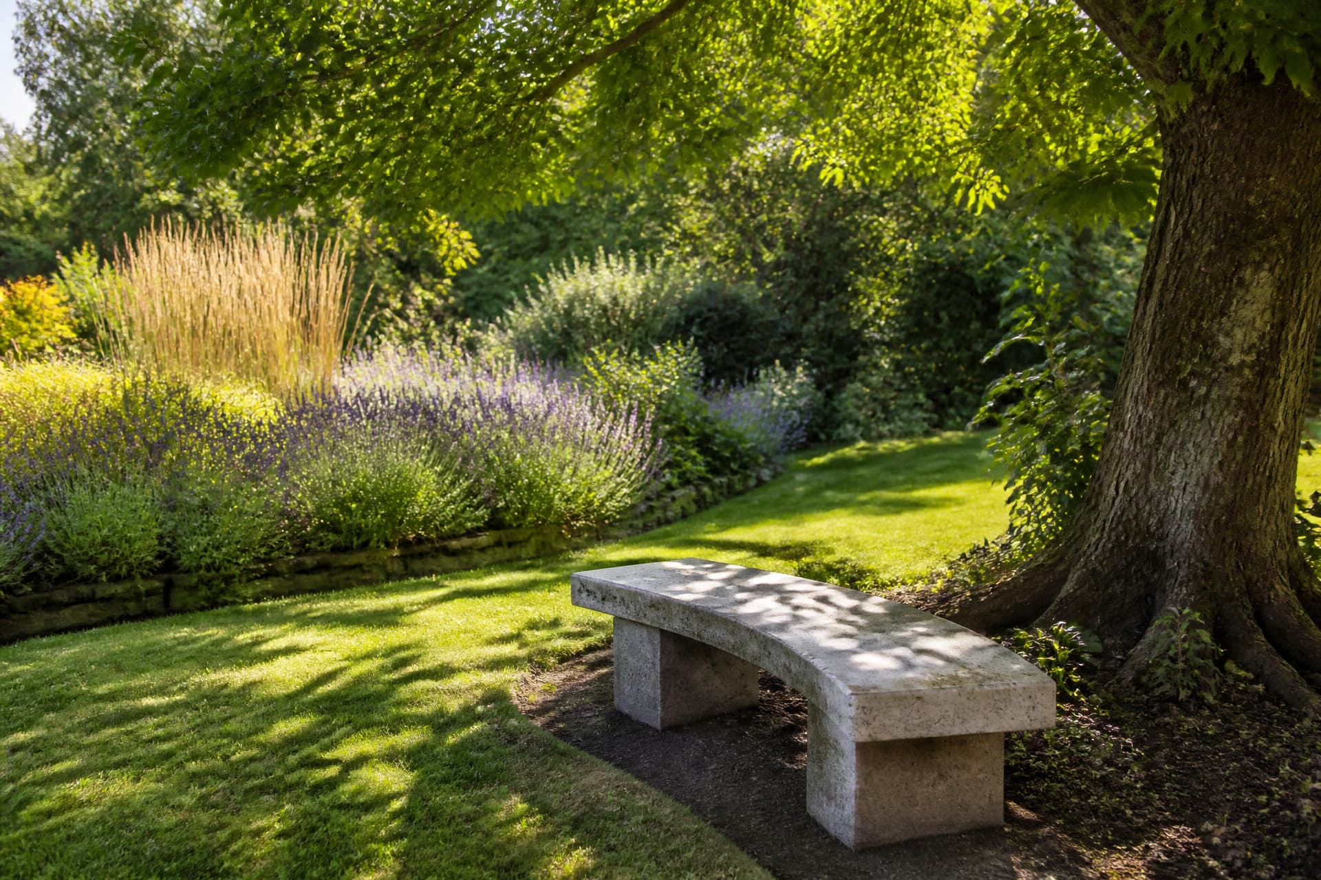 A curved granite memorial bench at the edge of a lawn under dappled light, facing a low planted bed