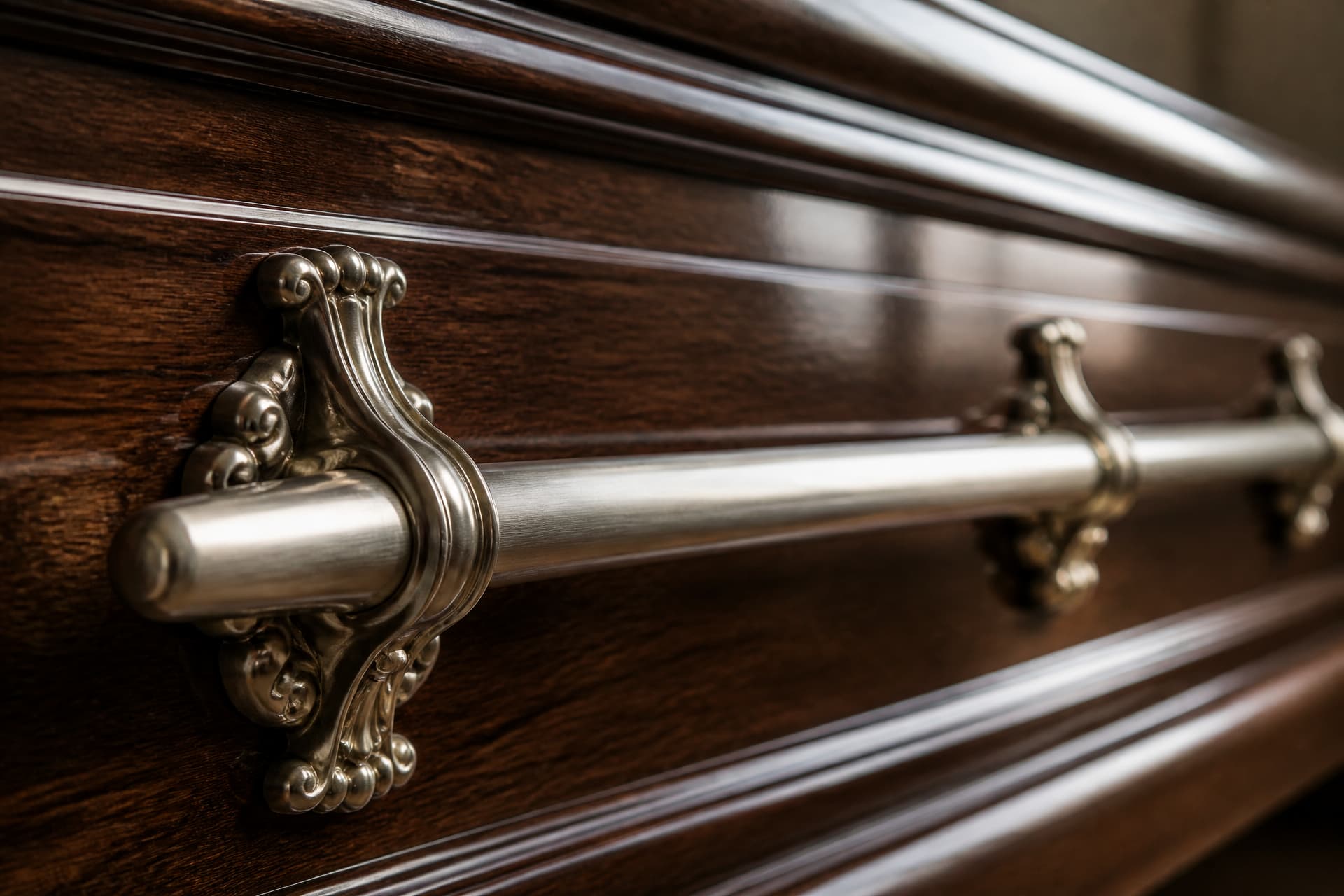 A close view of the polished side rail of a casket, a continuous metal bar mounted on decorative brackets along its full length