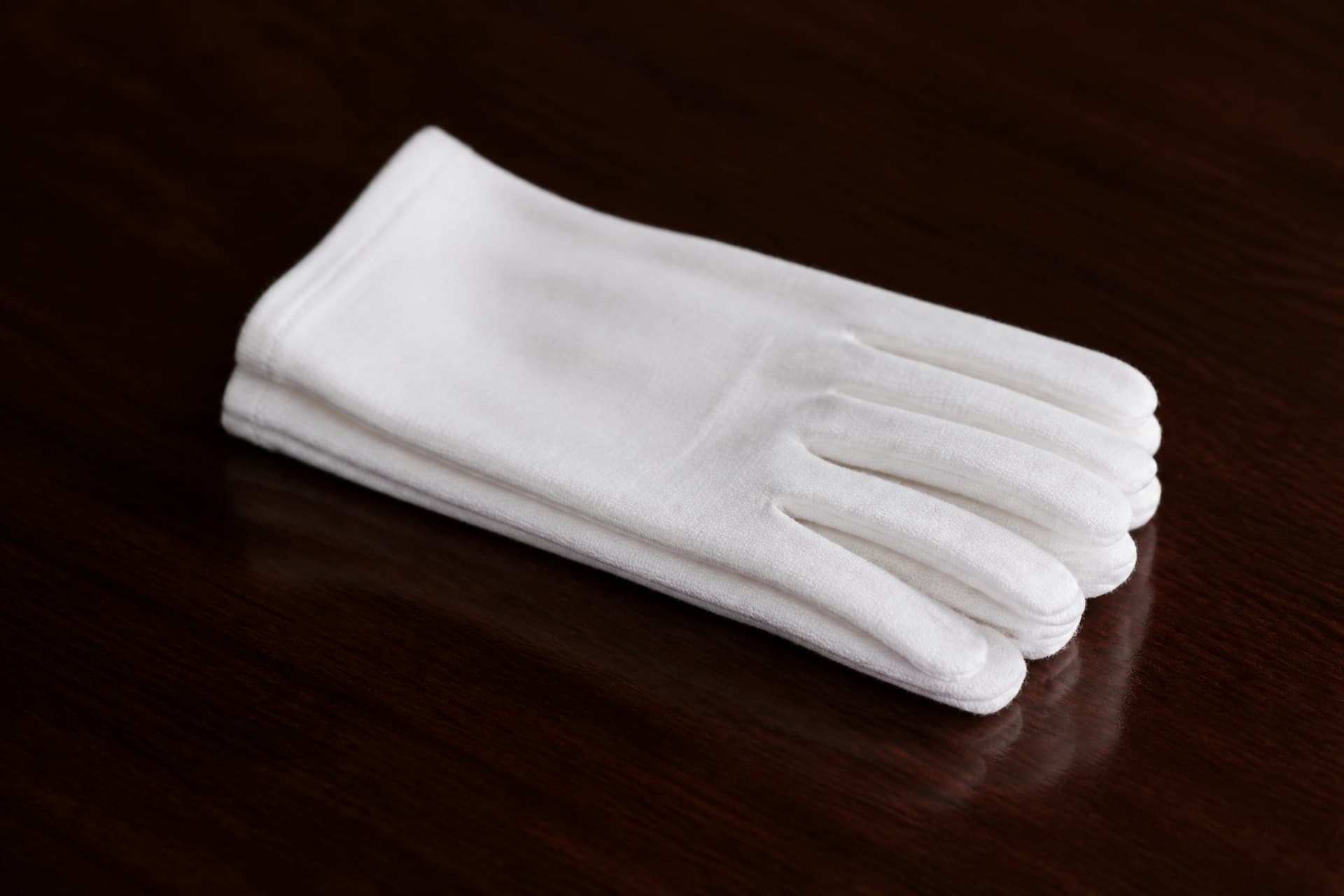 A neatly folded pair of white cotton gloves resting on a dark polished wooden surface