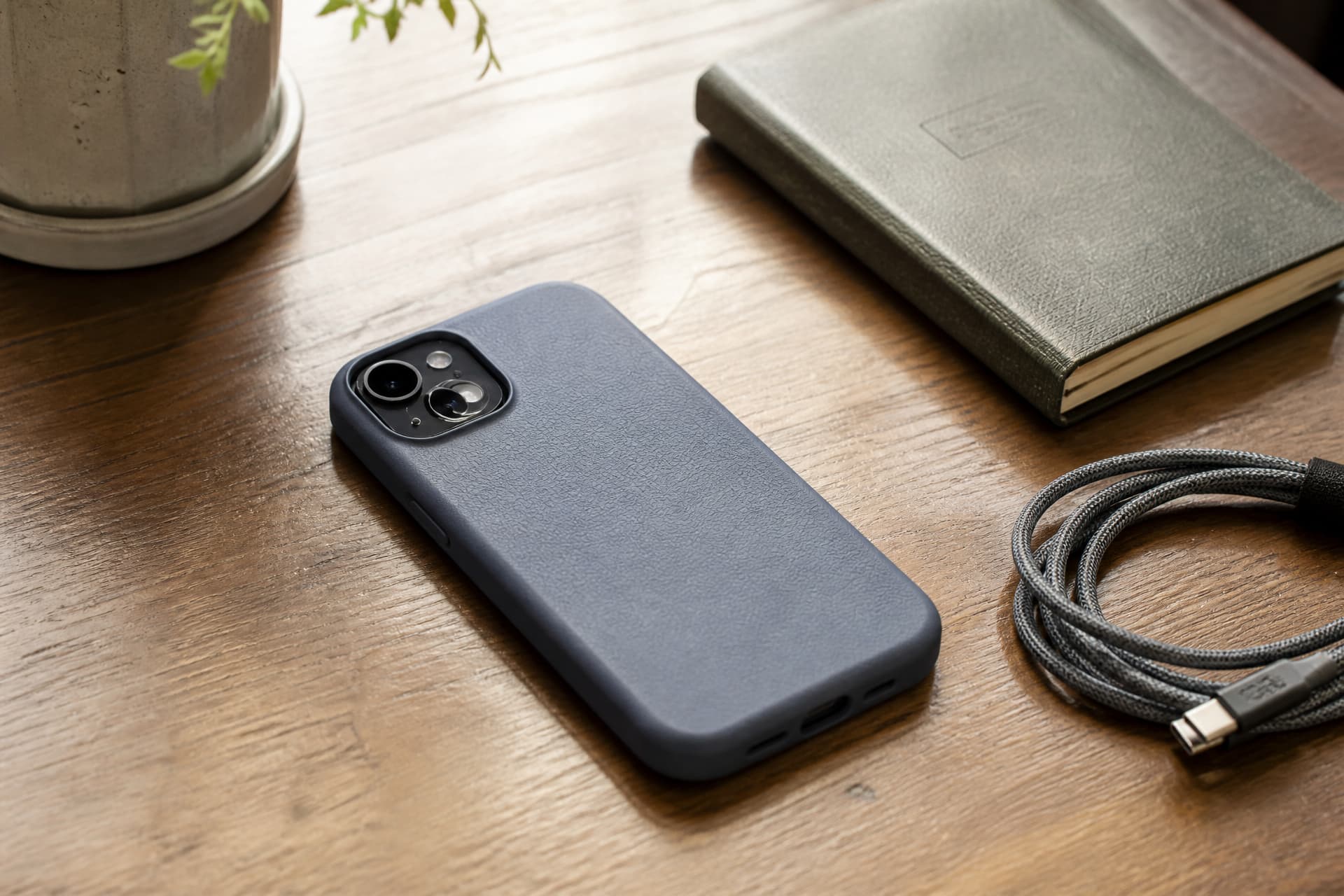 A smartphone lying face-down on a wooden table beside a coiled charging cable and a small notebook, warm daylight