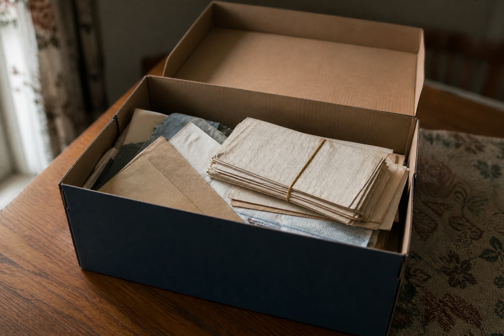 An open shoebox on a table holding old envelopes, folded documents and a rubber-banded bundle of papers, warm indoor light