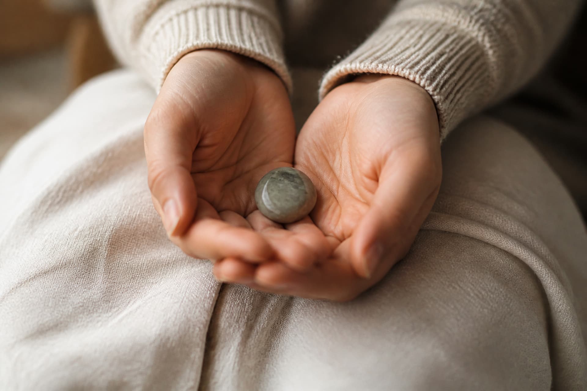 A pair of cupped hands holding a smooth polished comfort stone resting in a lap