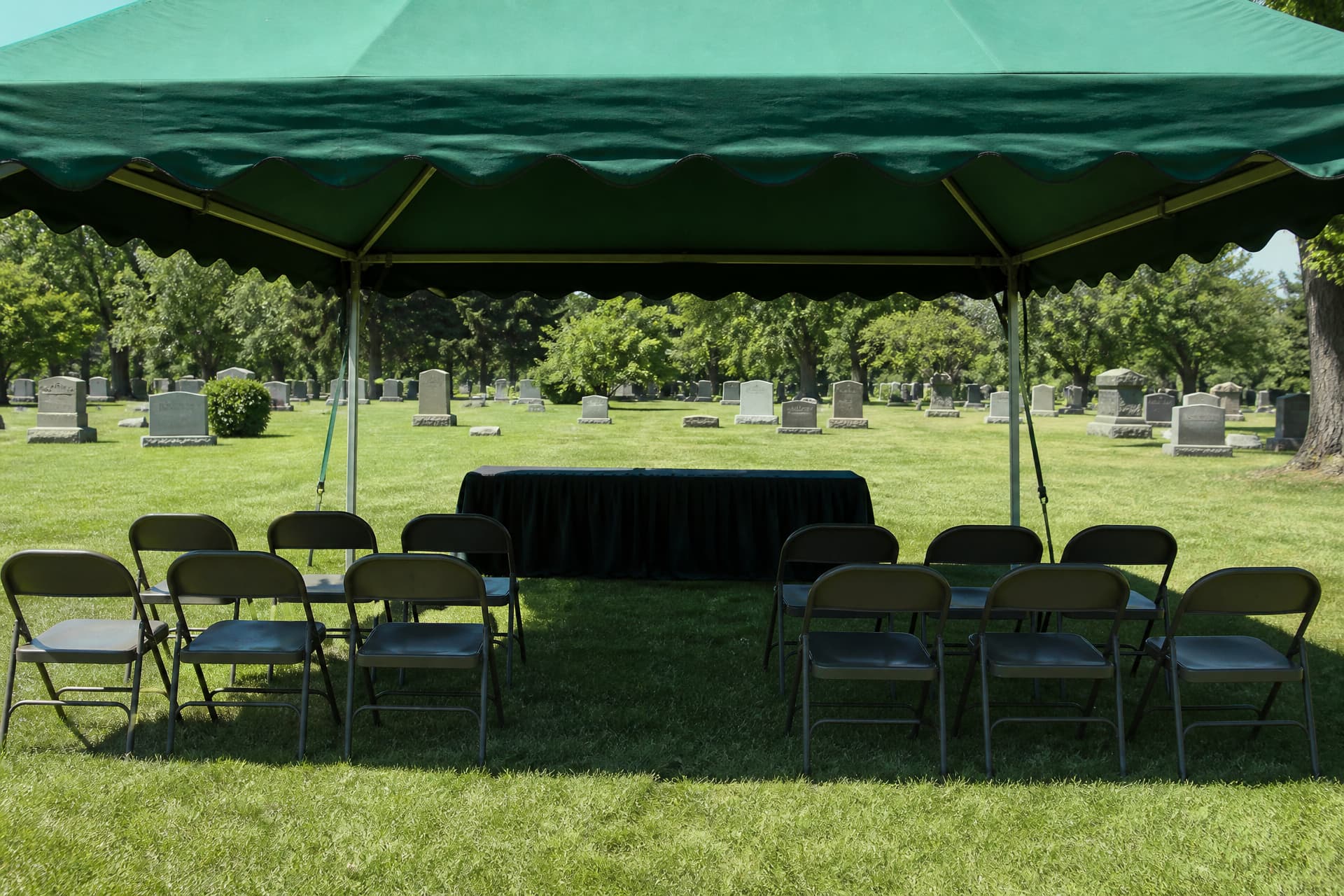 Rows of chairs arranged under a canopy at a graveside on a bright summer day