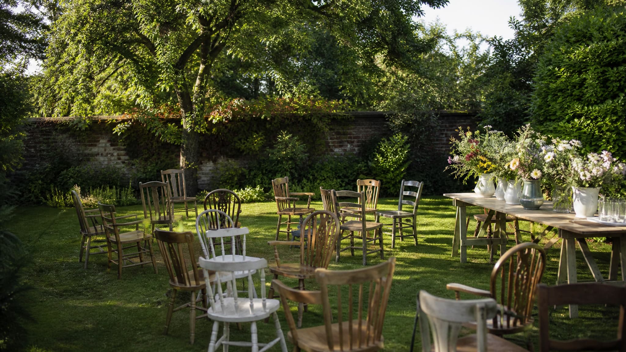 A garden set up for a memorial gathering with empty wooden chairs and bright summer flowers in the afternoon sun