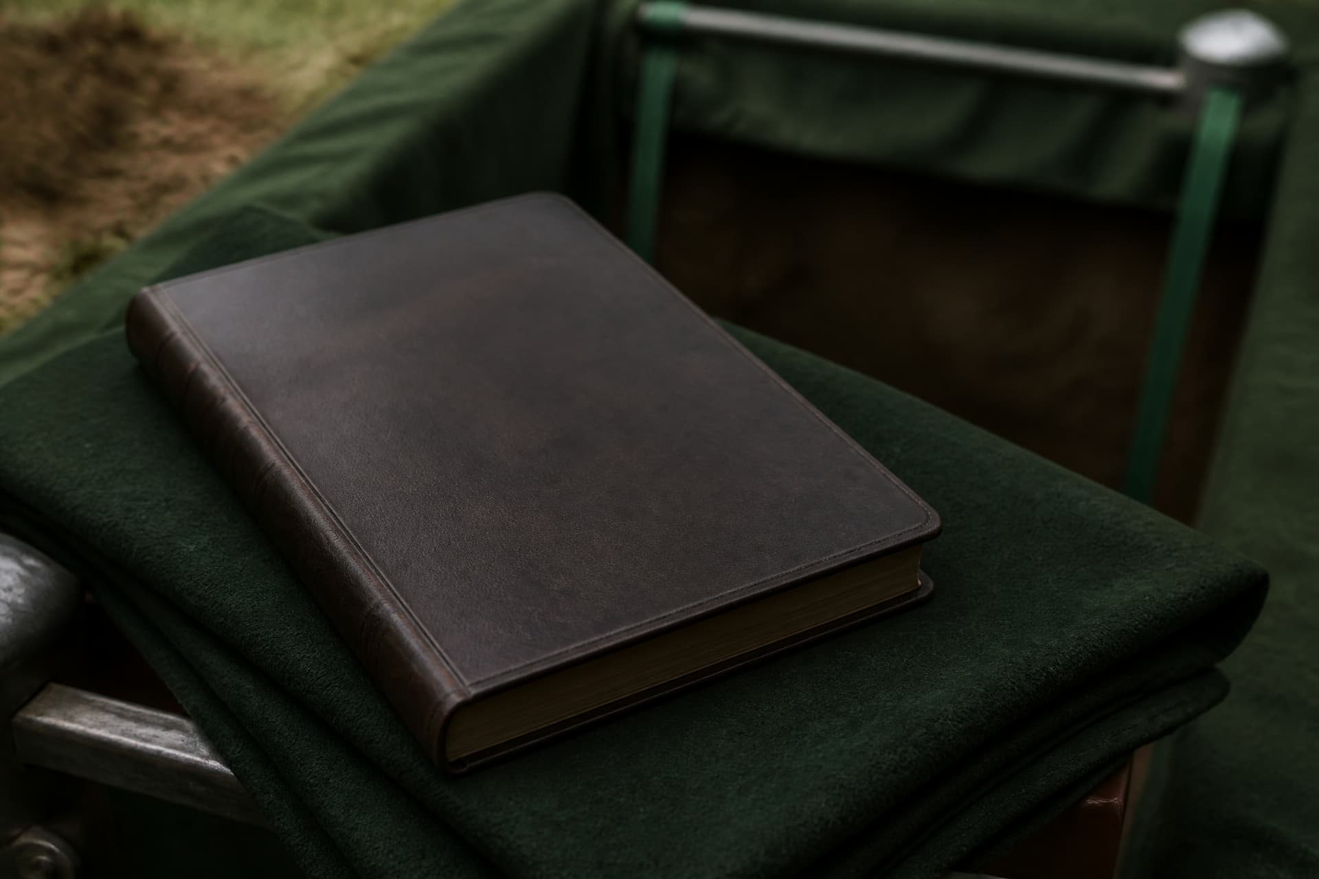 A closed leather-bound service book resting on folded green cemetery cloth at the edge of an open grave