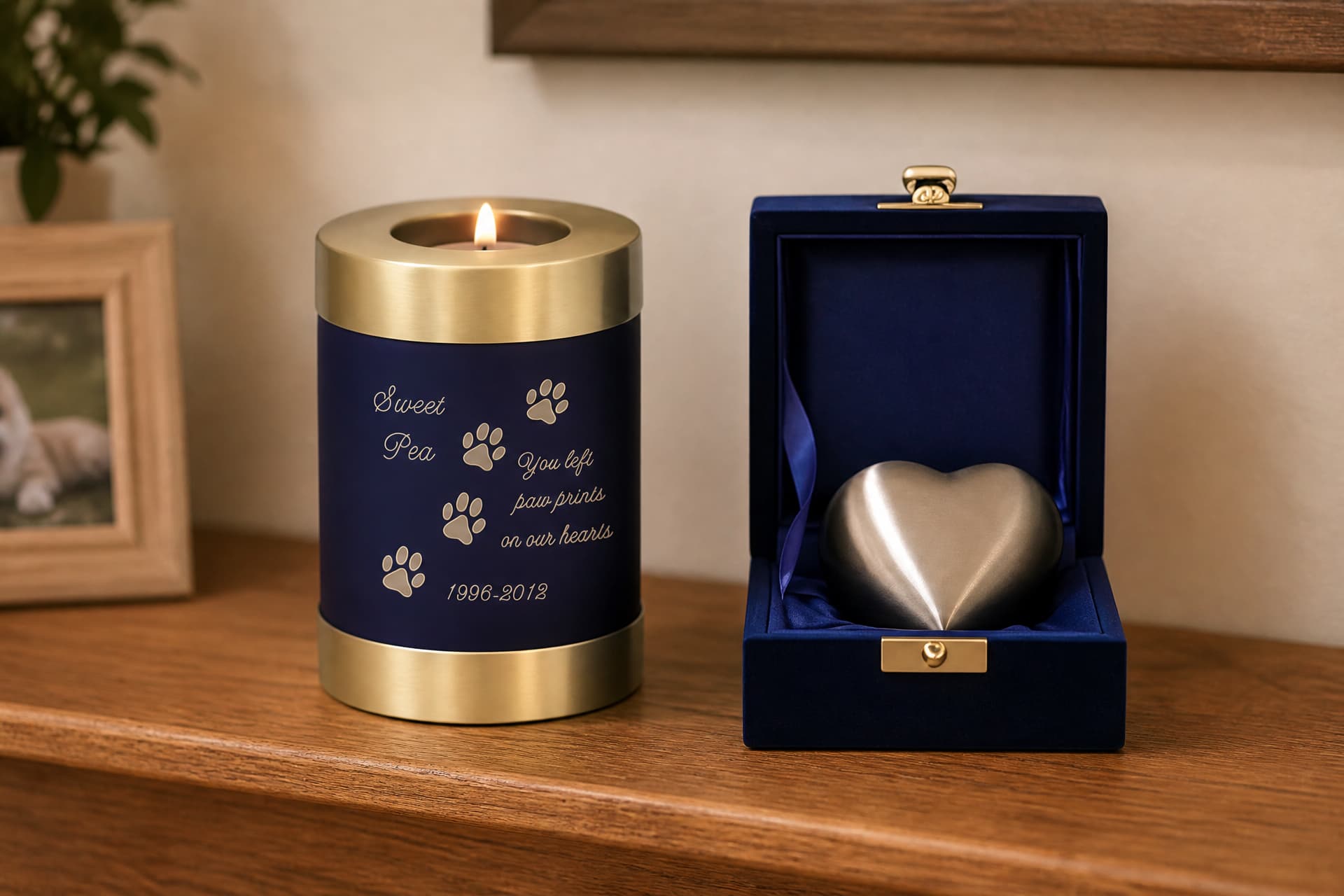 Two small pet keepsake urns on a wooden shelf โ a navy candle-holder urn engraved with paw prints, and a pewter heart urn in its velvet presentation box