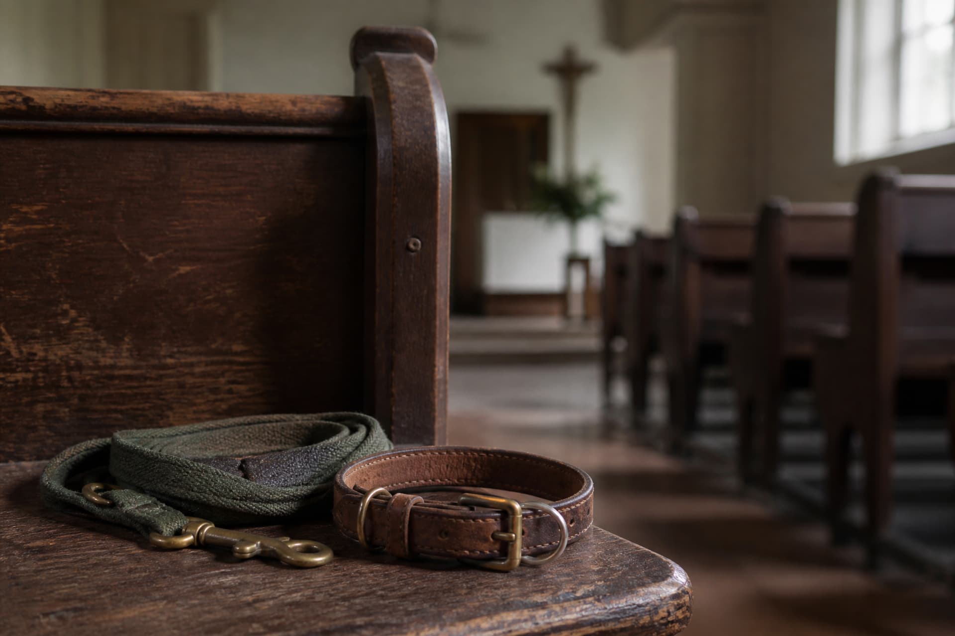 A leather dog collar and folded lead resting on a wooden church pew in an empty chapel