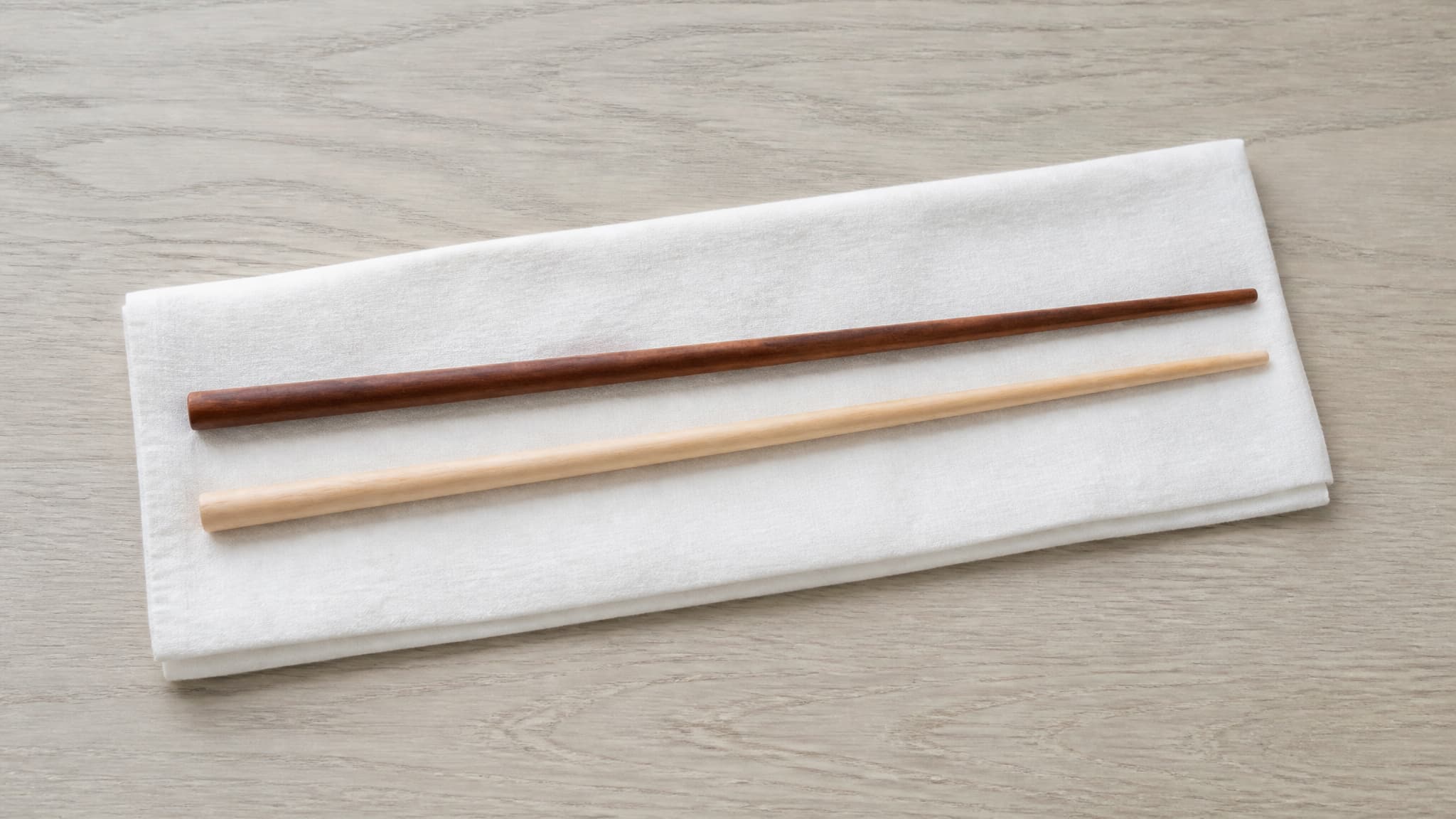 A pair of long ceremonial chopsticks resting on folded white cloth on a pale wooden surface