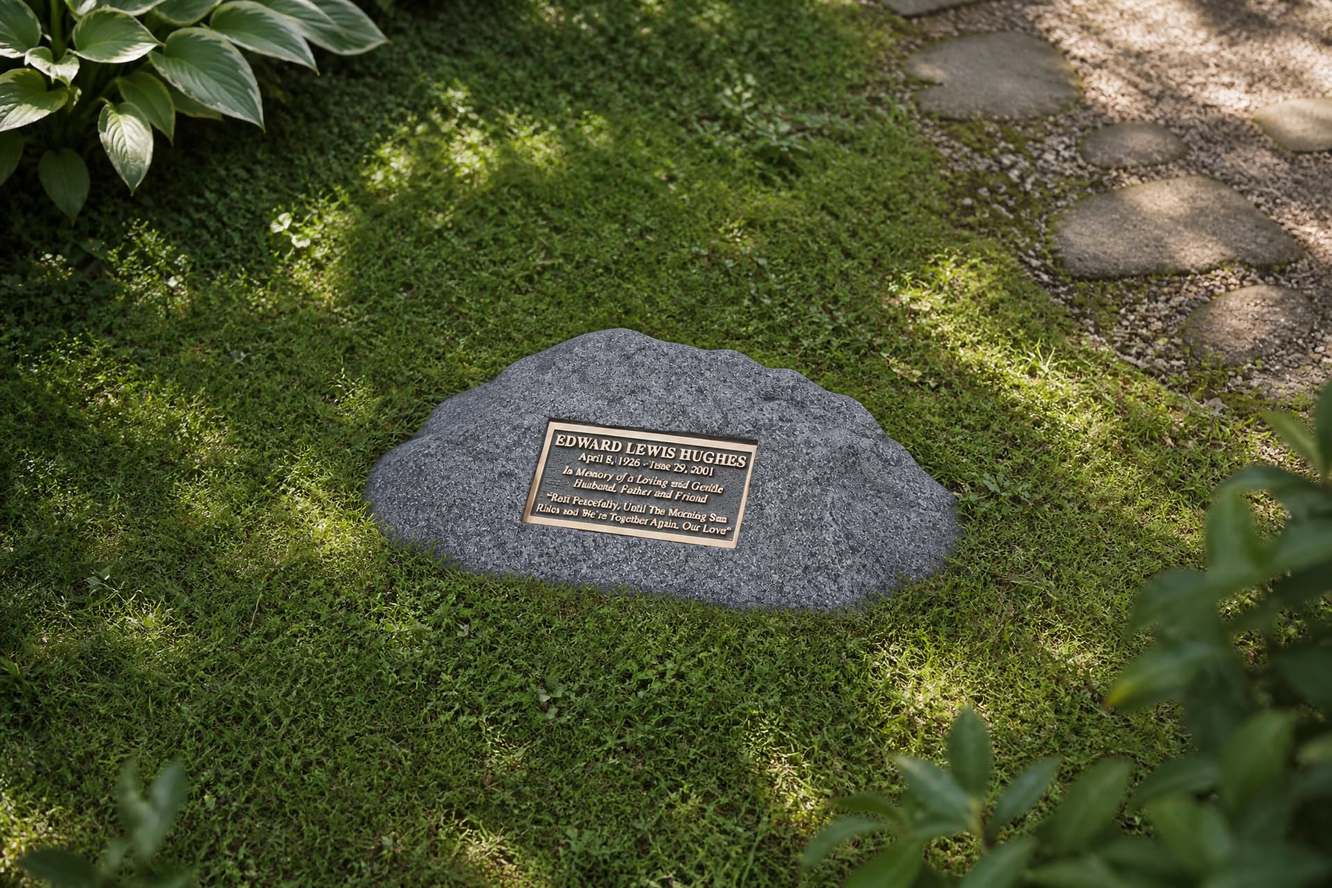 An engraved memorial garden stone with a bronze plaque, set flush in moss and low planting beside a stepping-stone path in dappled light