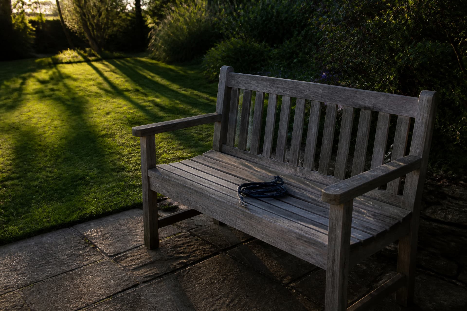 An empty wooden garden bench in evening light with a folded dog lead on the seat