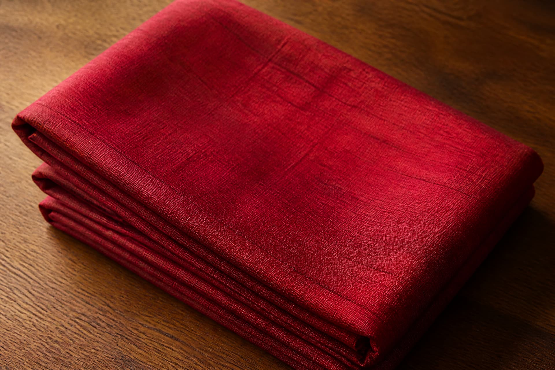 A length of deep red hand-woven silk cloth folded neatly on a bare wooden table in soft natural light