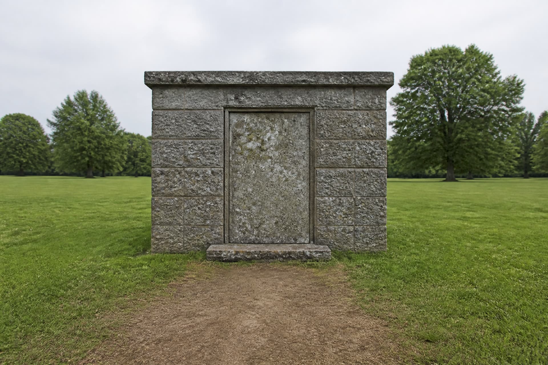 The stone doorway of an old above-ground tomb with the grass in front of it worn bare by repeated visits