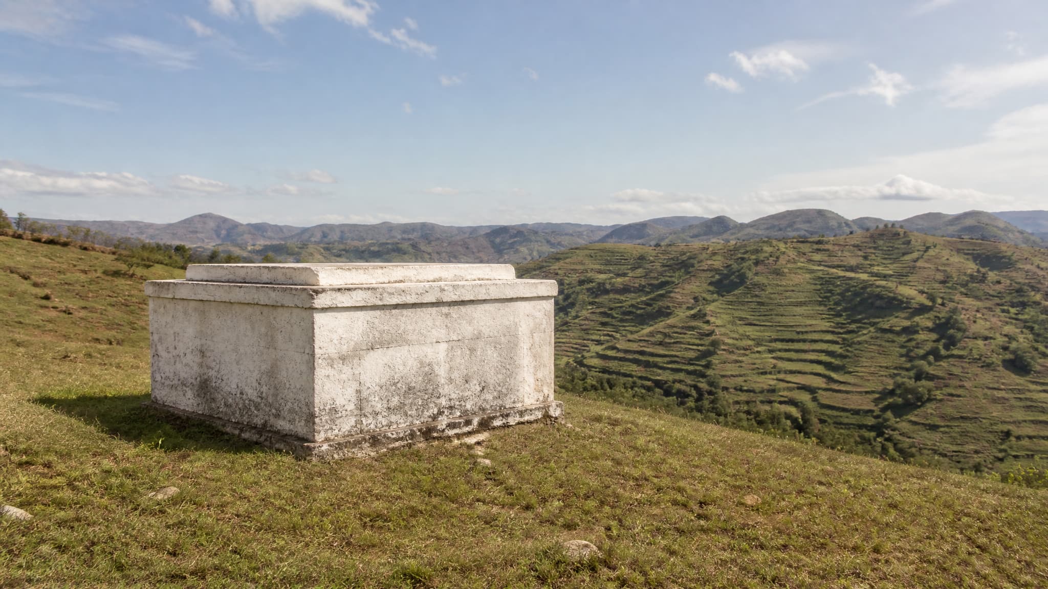 A whitewashed stone family tomb standing alone on a grassy highland hillside in Madagascar under clear dry-season light