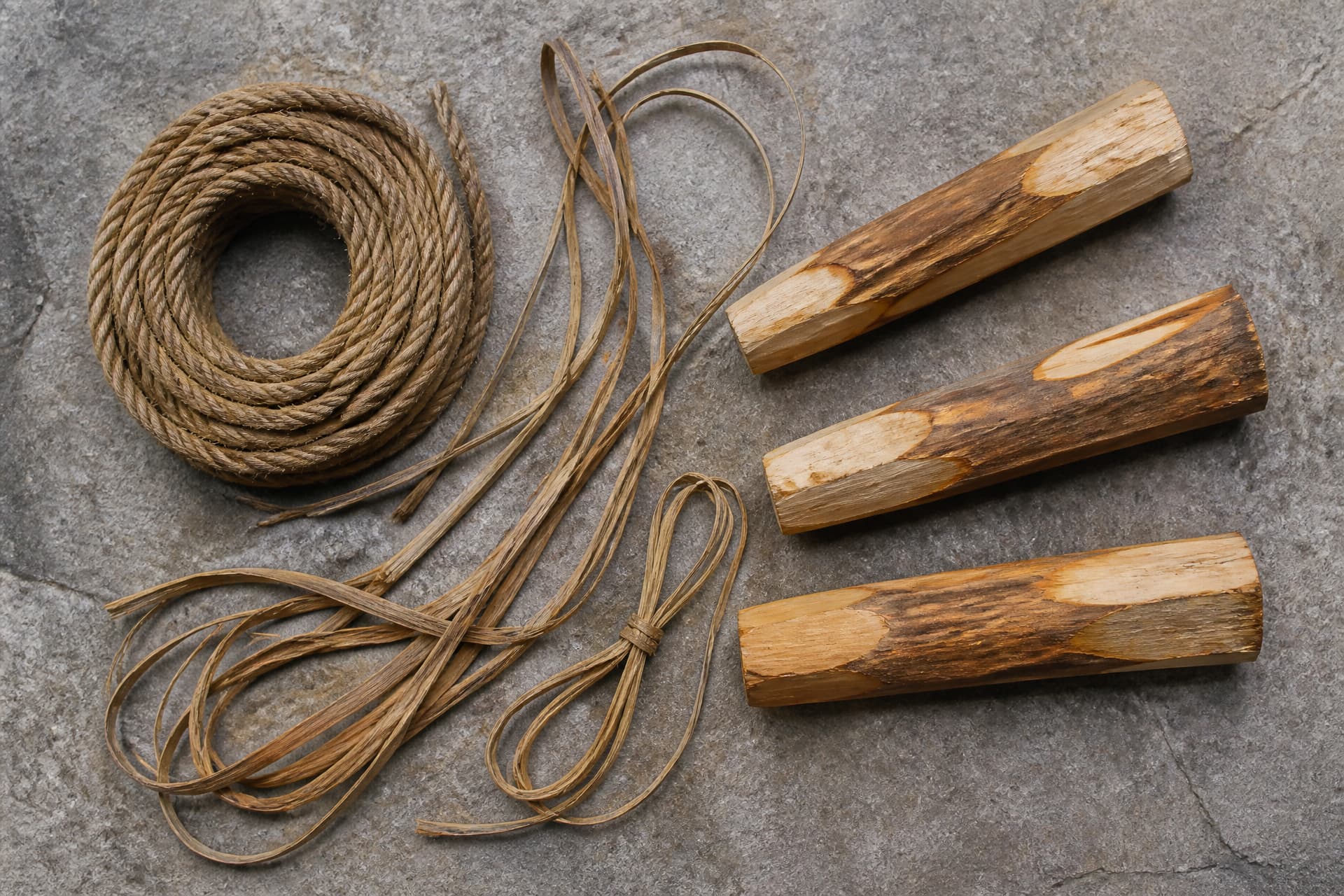 Coils of rope and rattan lashing laid out beside lengths of split timber on a flat stone surface, photographed from directly above