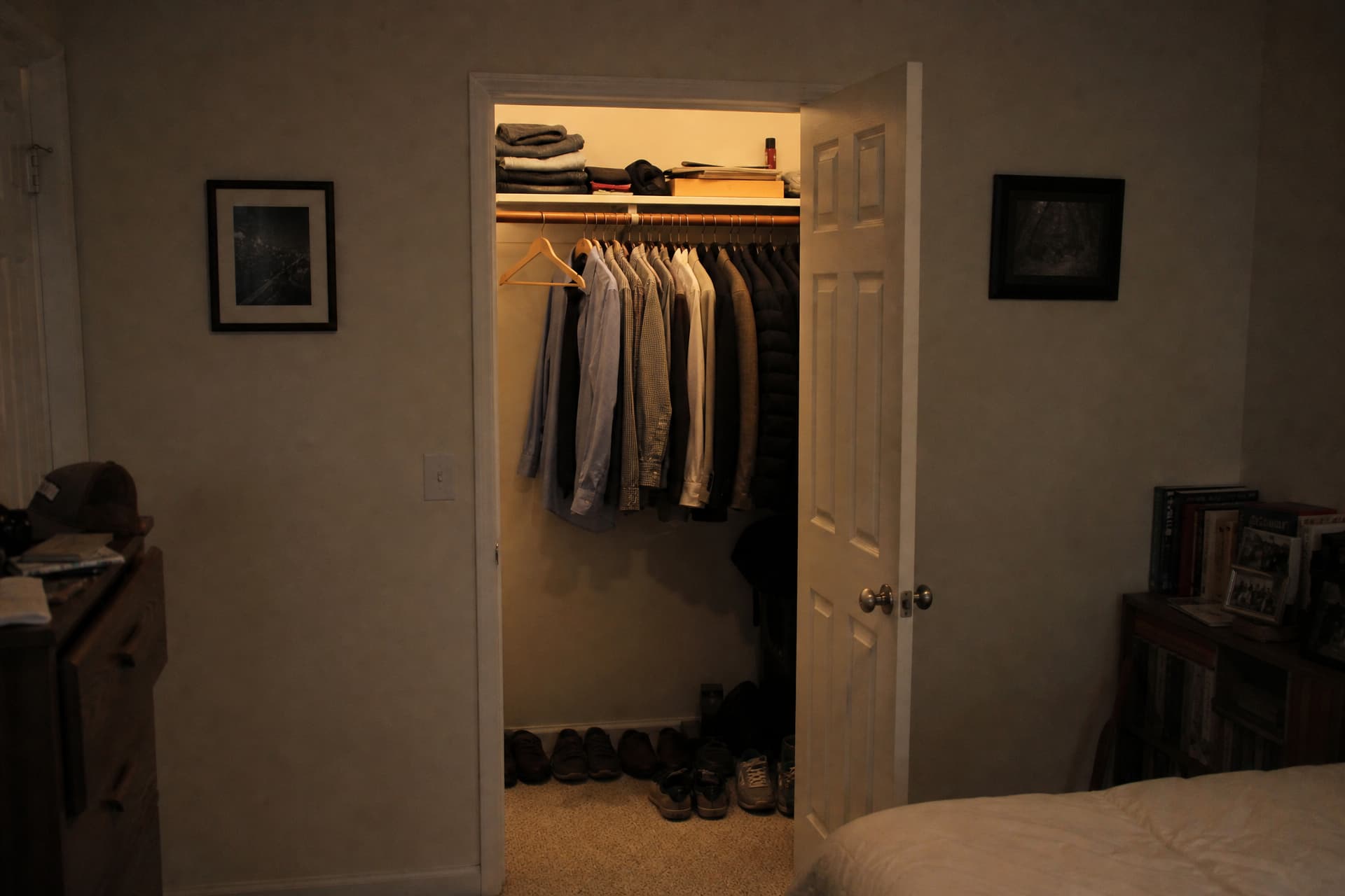 An open closet with half the rail still full of hanging clothes and a single empty wooden hanger at the front, the room dim and the closet lit from inside