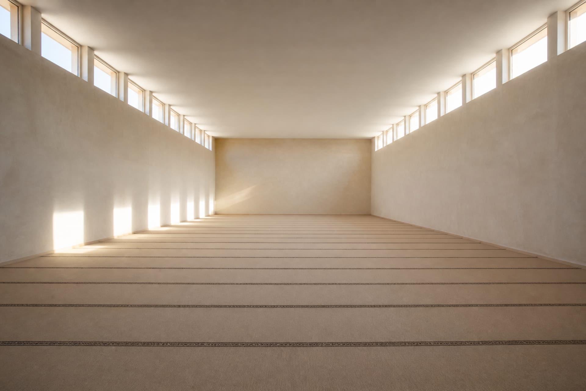 An empty carpeted prayer hall with straight rows woven into the carpet and daylight falling across it from high windows