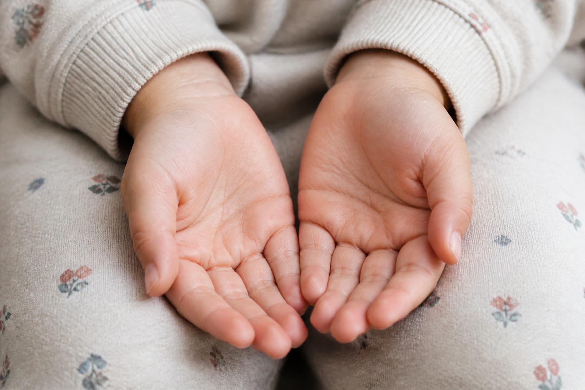 A child's empty cupped hands resting in their lap, close crop