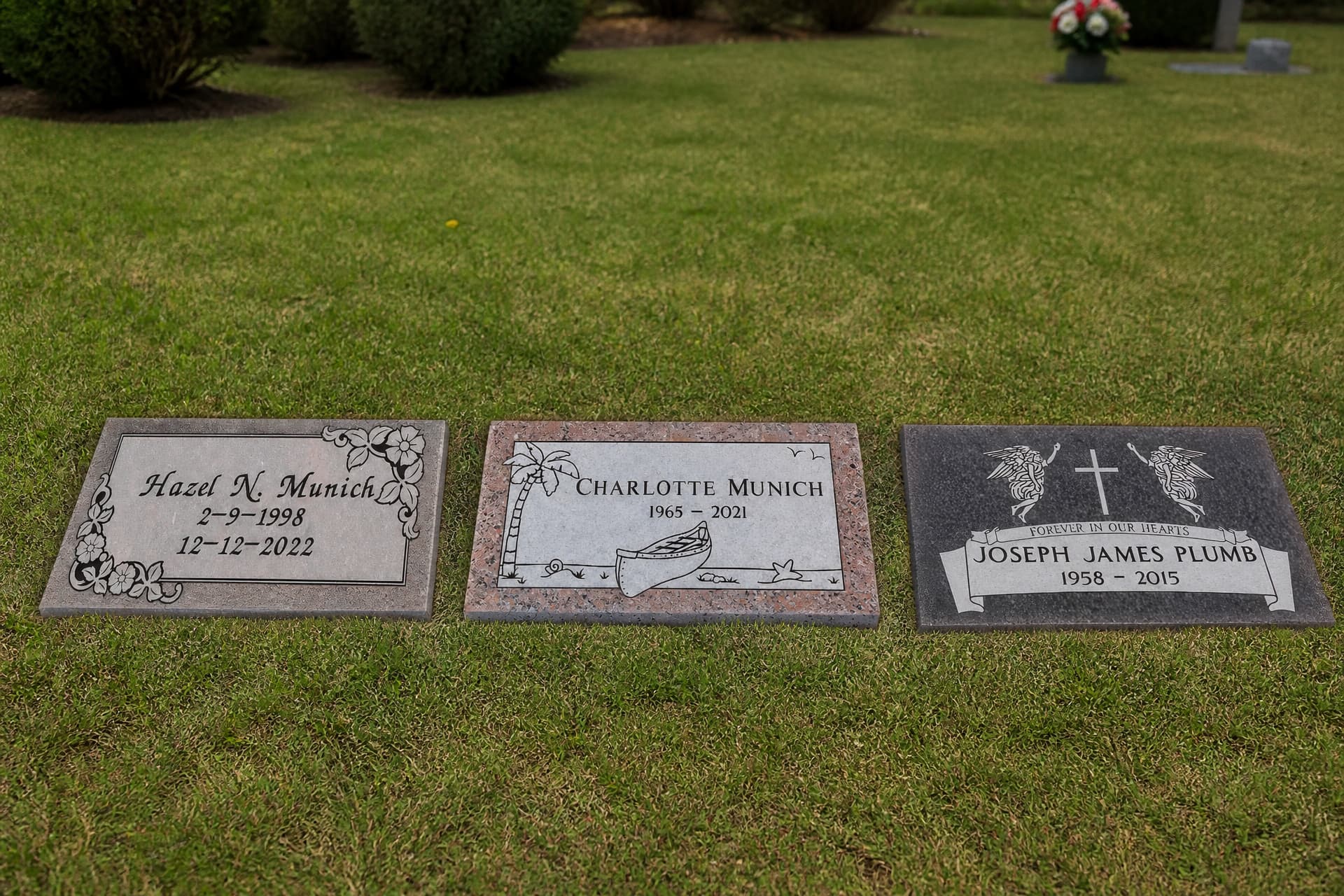 Three flat granite grave markers lying face up in mown cemetery turf, photographed from an elevated angle so each engraved name and pair of dates is legible