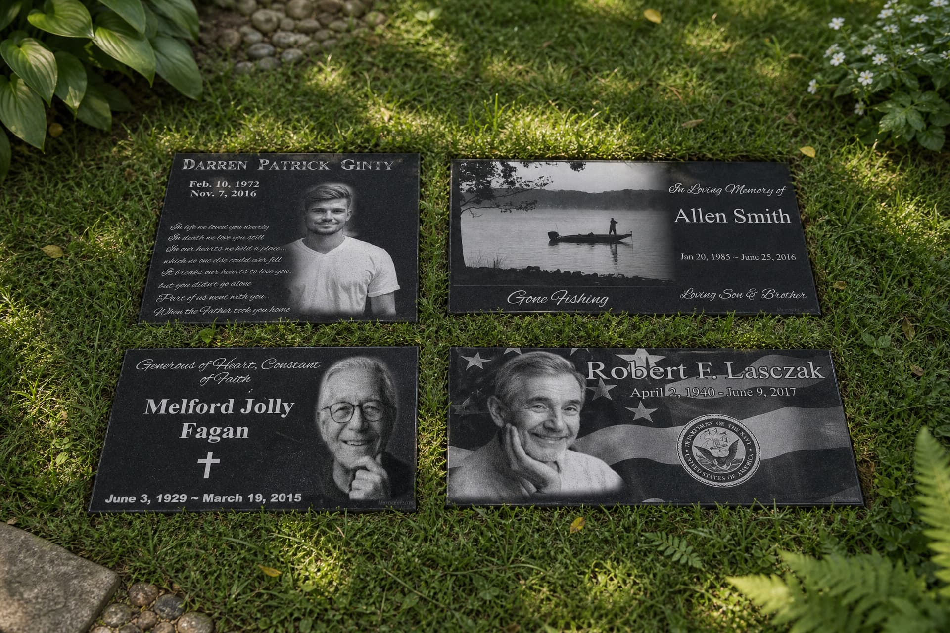 Four polished black granite memorial stones laid on grass among garden planting, each laser etched with a portrait or a scene alongside a name, dates and an inscription