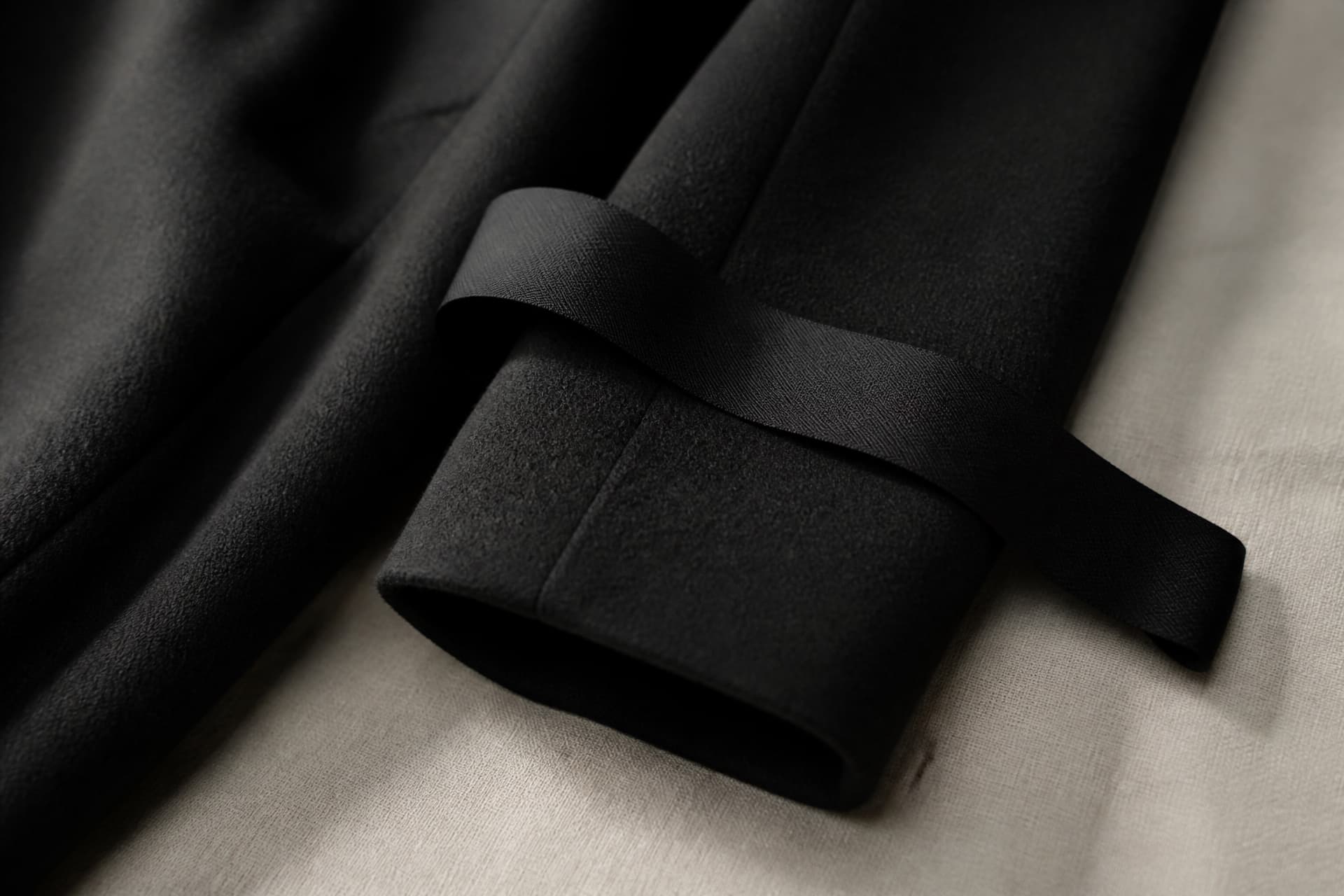 A black fabric mourning band resting on the sleeve of a dark wool coat on a pale linen surface