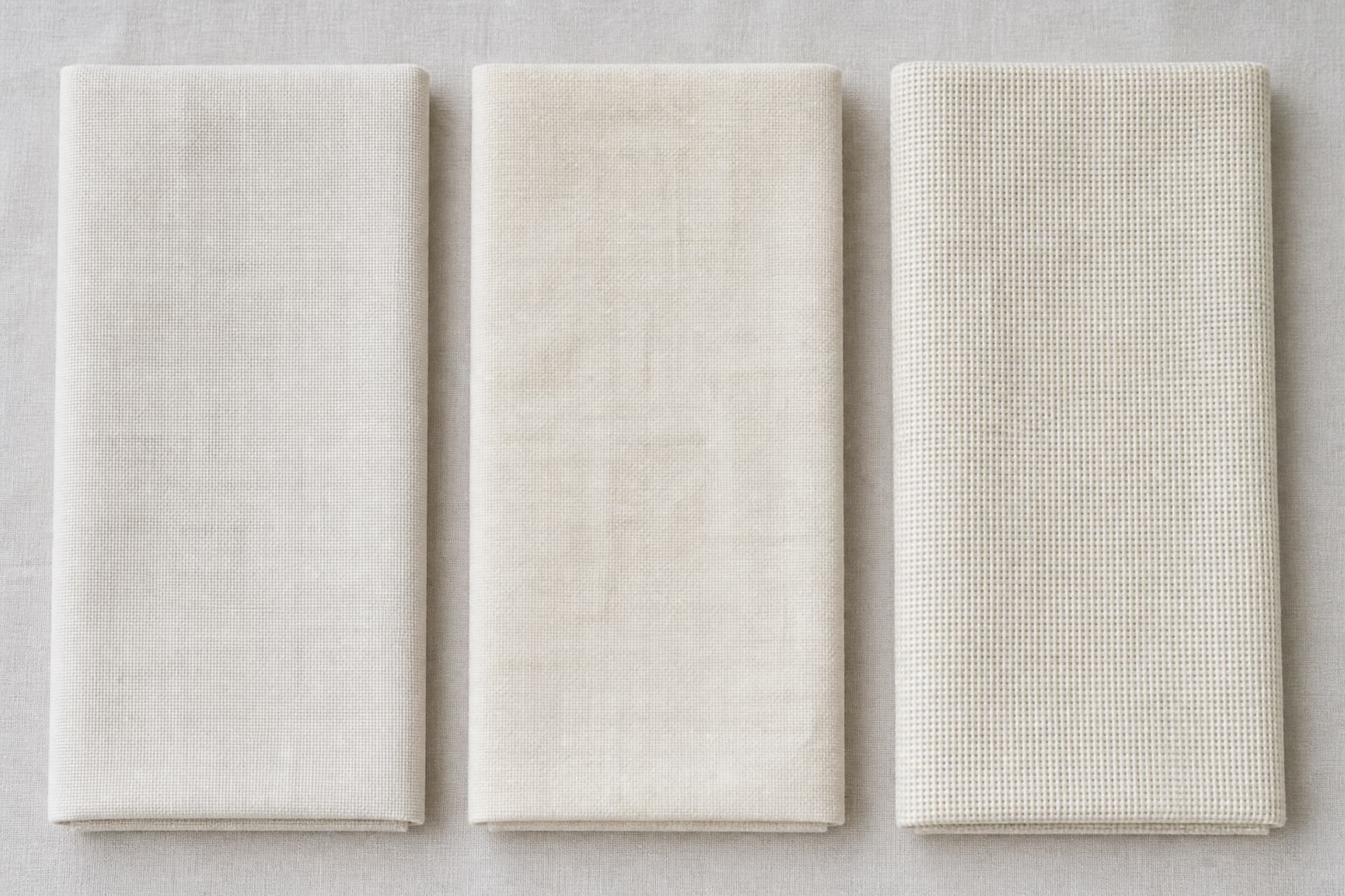 Three folded lengths of plain white cloth in slightly different weaves laid side by side on a neutral surface