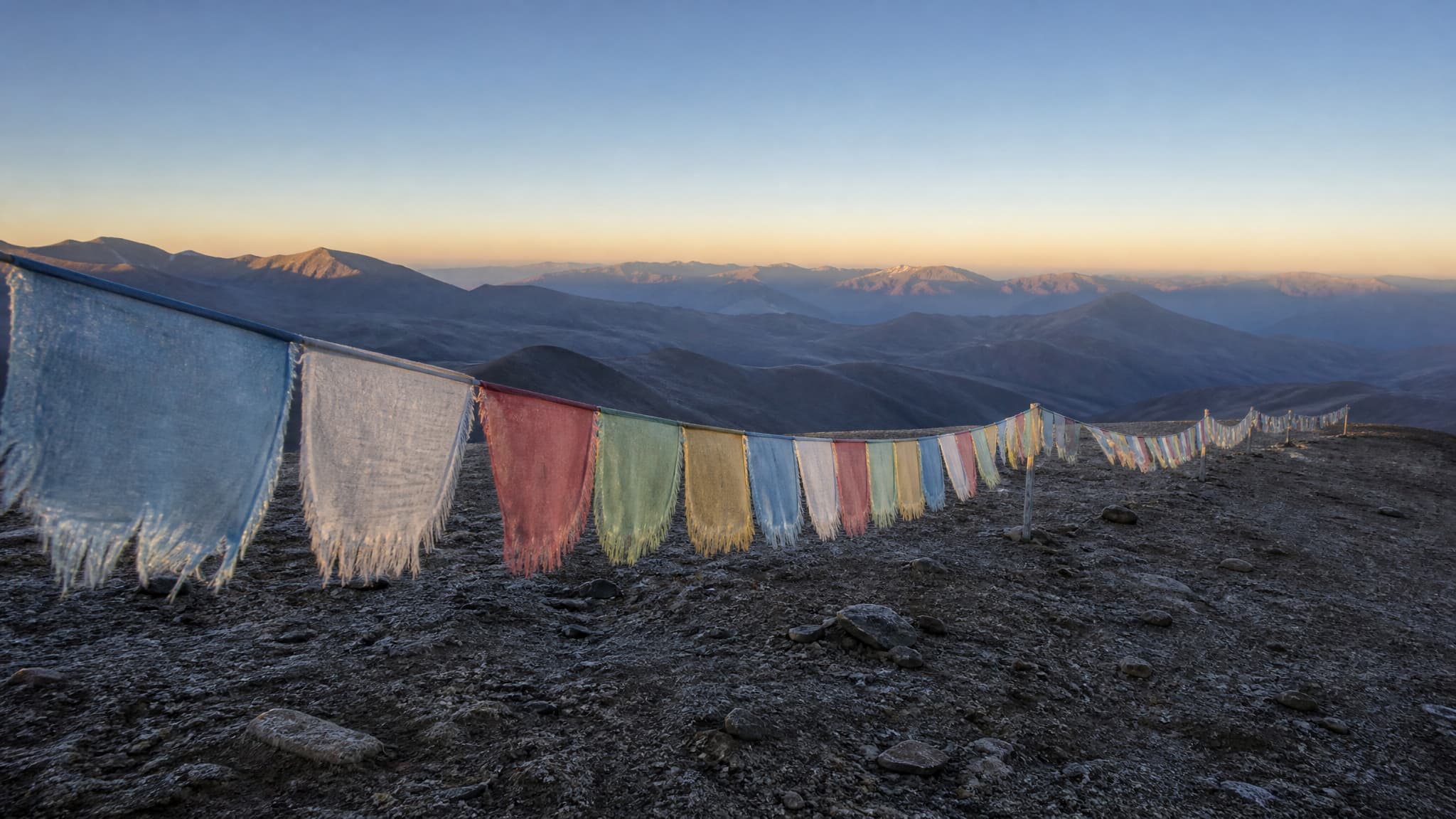 Weathered prayer flags strung across a ridge on a high, treeless plateau at first light, with open sky beyond