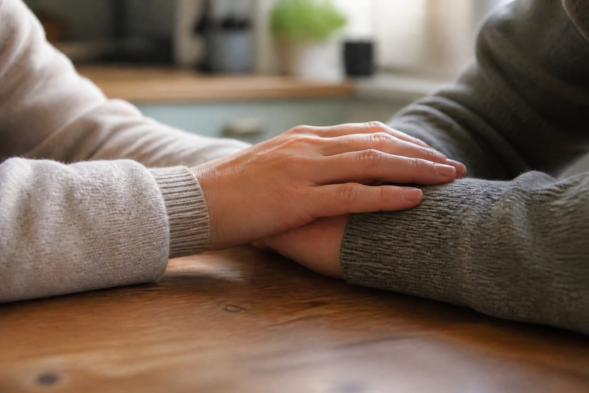 A hand resting on someone's forearm across a kitchen table