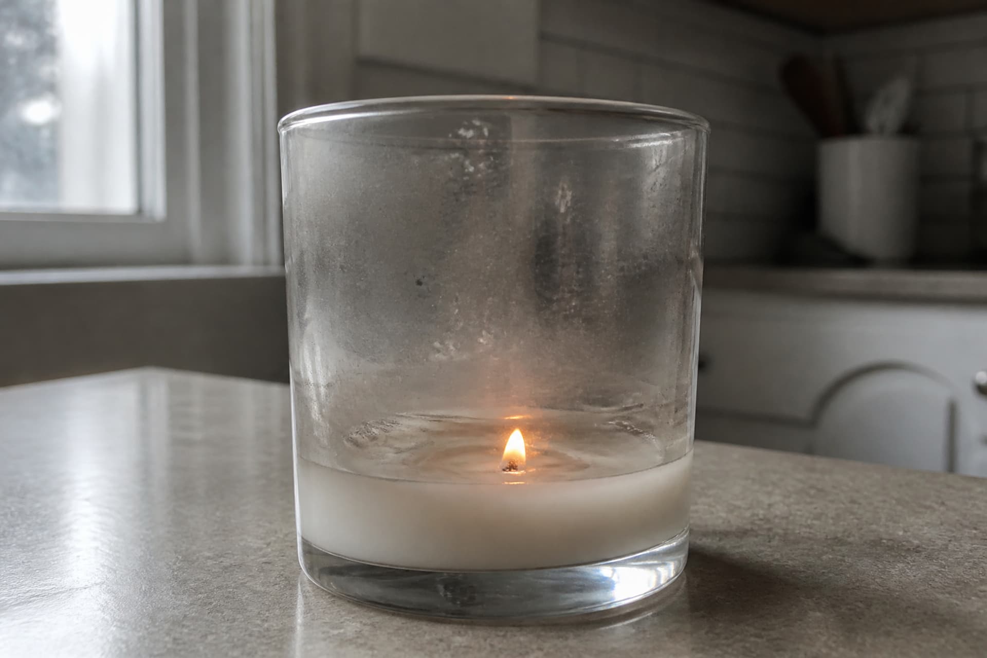 The same jar candle the following morning, burned two-thirds down with cloudy pooled wax and a small flame, in flat gray daylight