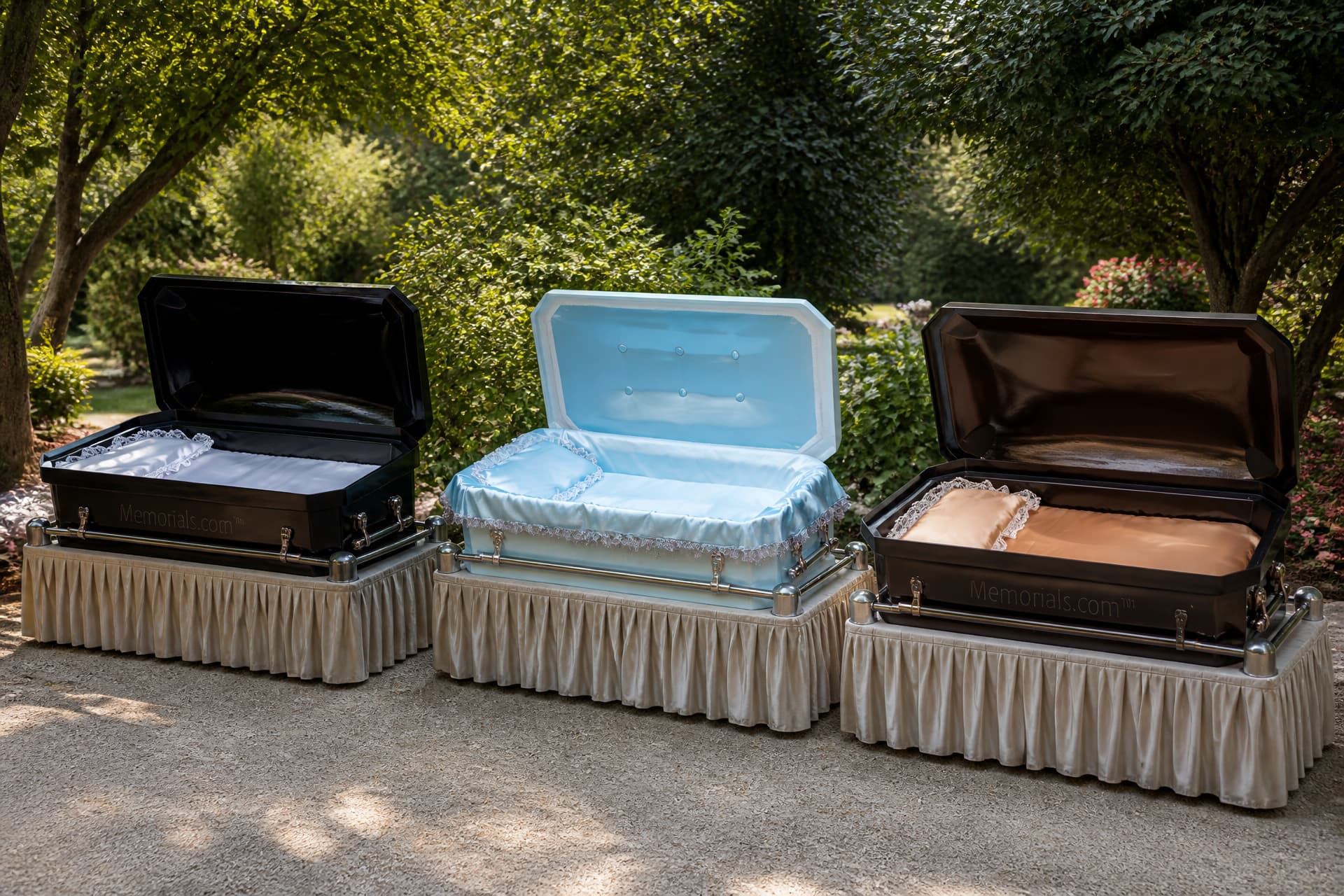 Three open pet caskets on black-draped biers on a garden path in dappled daylight, the left lined in white satin, the center in tufted pale blue and the right in bronze, each with chrome rails along the sides